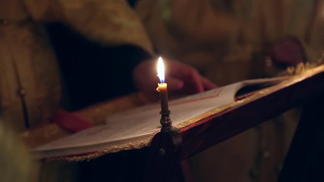 An orthodox priest in the church prays and crosses himself in the dark by candlelight
