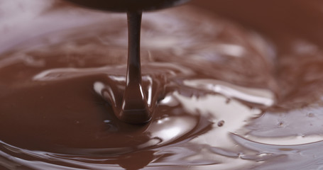 Slow motion of premium dark melted chocolate being poured from spoon in center part of frame, 4k photo