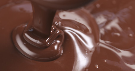 Slow motion of premium dark melted chocolate being poured from spoon in left part of frame, 4k photo