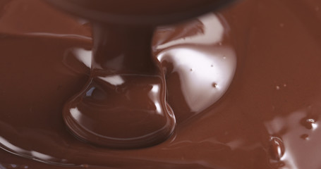 Slow motion of premium dark melted chocolate being poured from spoon in left part of frame, 4k photo