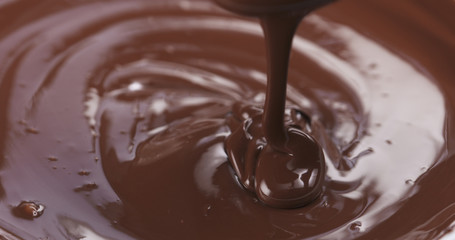 Slow motion of premium dark melted chocolate being poured from spoon in right part of frame, 4k photo