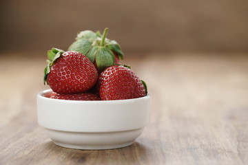 ripe organic strawberries in white bowl on wood table, with copy space