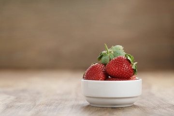 ripe organic strawberries in white bowl on wood table, with copy space