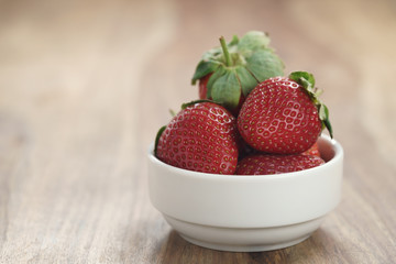 ripe organic strawberries in white bowl on wood table, with copy space