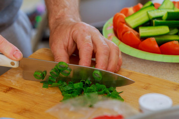Cut green onion with a kitchen knife on a wooden cutting board. Fresh green onions on a cutting board.