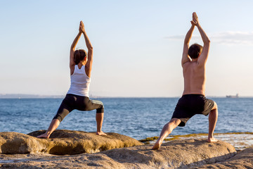Fototapeta na wymiar A couple is doing yoga exercises at the seashore of Mediterranean sea