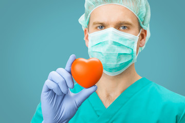 Medicine and healthcare - surgeon in green uniform holding toy heart with one hand