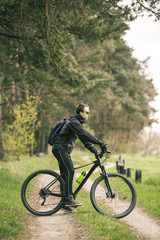 Fototapeta na wymiar Young attractive man wears dark suit ride the bike on the forest road