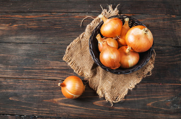 Raw golden onions in a basket on the wood table.