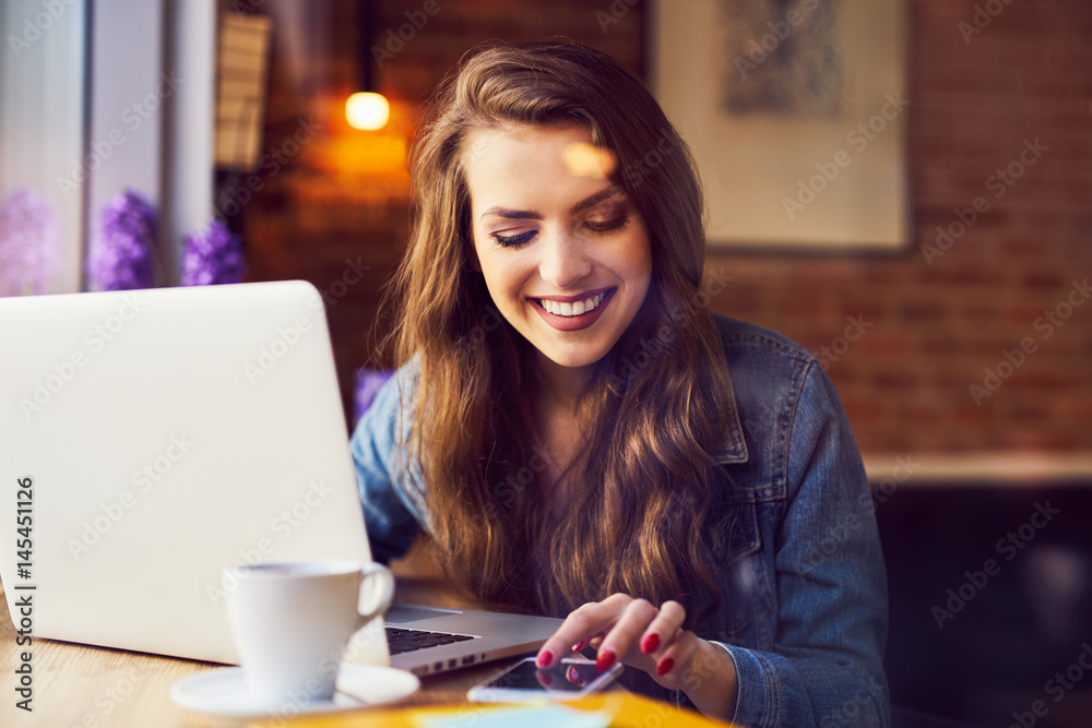 Wall mural happy woman with laptop at cafe checking her phone