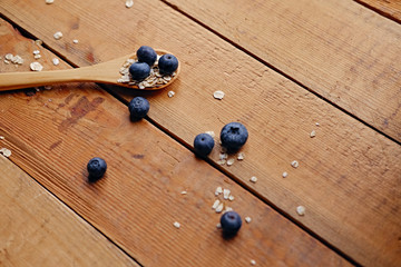 Wooden spoon with oat flakes and blueberry over wooden pattern background.