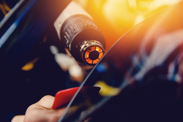 Master installs a tint film for the car glass with a hairdryer and spatula with glare of light....