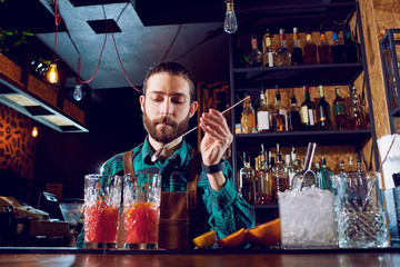 Bartender hipster with a beard makes  cocktail at the bar.