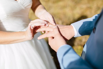 Bride in white dress and groom in a suit are putting rings on their hands. Wedding ceremony
