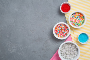 Colorful sprinkles for cupcakes and ice-cream in bowls on grey background and striped yellow and pink cloth. Copy space