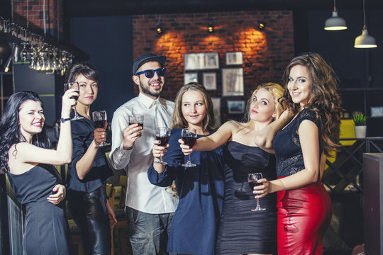 Young cheerful company of friends in the club bar having fun with alcohol in hand celebrate