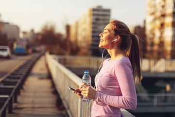 Happy young woman listening to music after jogging at sunset - obrazy, fototapety, plakaty