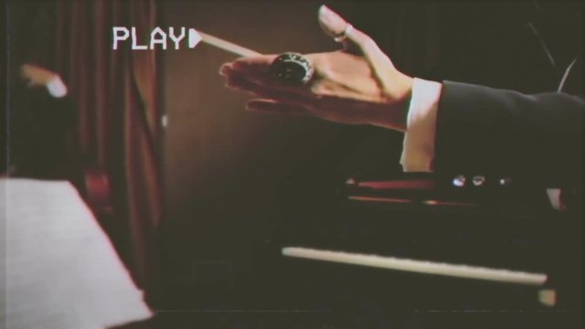 Fake VHS tape: the swinging hands and baton of the conductor of an orchestra (ensemble of musicians). Conducting: directing a musical performance with visible gestures.
