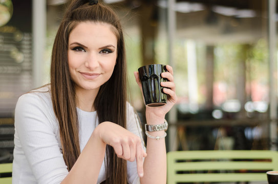 Beautiful young manager drinking coffee after work and pointing with fingers below, click here