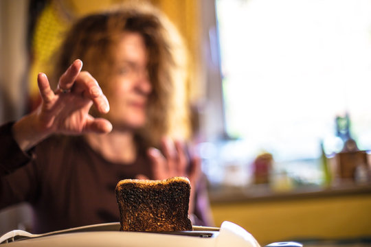 eine Frau greift nach einer verbrannten Scheibe Brot in einem Toaster