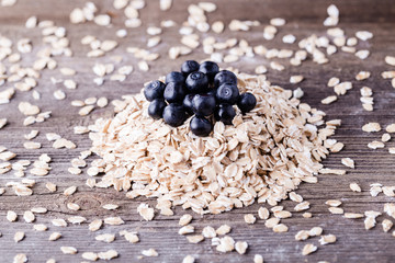 Raw oat with blueberry on top on wooden background.