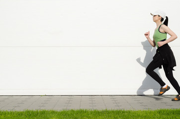 Girl in sports clothes race in front of a blank white wall