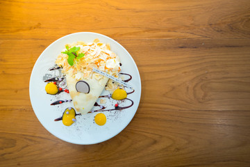 Coconut creamy crape with crispy almond in decorated white ceramic plate on rustic wooden table.