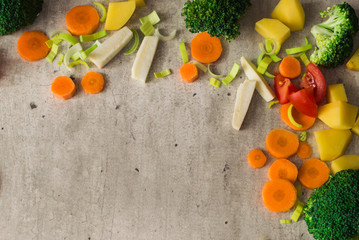 Carrots, broccoli, parsley root, leek, tomato and potatoes on a wooden cutting board gray stone background.