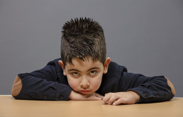 Fototapeta premium Small student boy sitting on wooden table