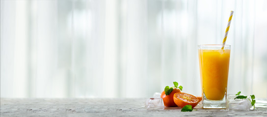 Fresh tangerine juice in glass on white concrete background. Orange fruits with ice, mint. Cold beverage for hot summer day. Copyspace. Banner.