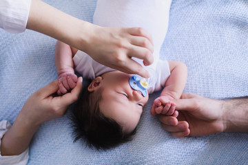 Parents with Newborn Baby Boy. Hand corrects the pacifier to the child. Top shot.