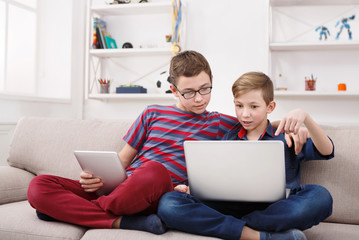 Fototapeta premium Two teenage boys using tablet on couch at home