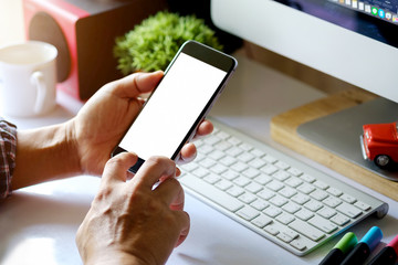 Man using smartphone with Designer workspace and stuff on White Desk. Blank screen smartphone for graphic display montage.