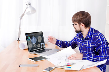Cad engineer's workplace with laptop, drawings, notepad and pen, smartphone and lamp. Young...