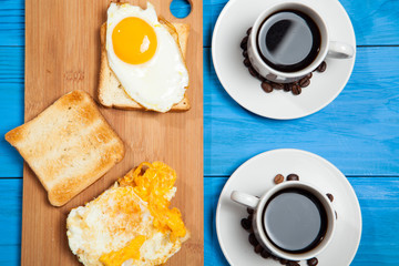 Two cups with coffee, toast and egg on a blue wooden table