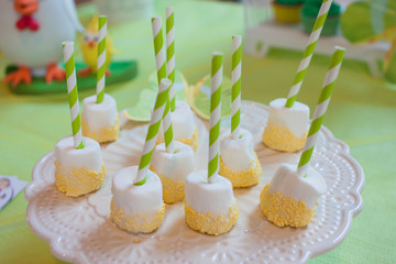 Cake pops on striped white-green tubes, from white meringue in yellow decorative balls on the table of candy bar