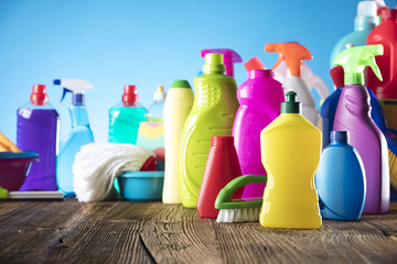 Spring cleanup theme. Variety of colorful house cleaning products on a rustic wooden table and blue background. 