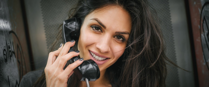 Happy and smiling woman talking in the retro phone booth