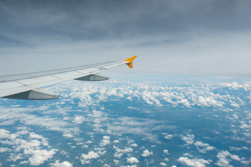 Wing of an airplane flying above the clouds see through the window. Business concept.