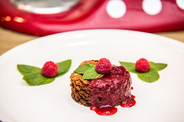 A chocolate cupcake with chocolate frosting served with fresh ripe raspberry.