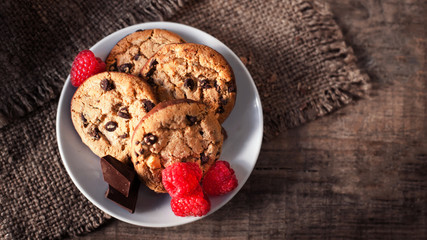 Chocolate chip cookies on white plate dark old wooden table with red raspberry and  place for text.,  freshly baked. Selective Focus with Copy space..