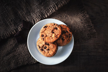 Chocolate chip cookies with chocolate pieces on white plate dark old wooden table .
