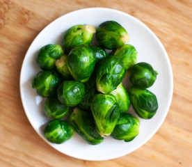 Pile of Fresh Green Brussels sprouts on a white plate on wooden table  with copy space, close up