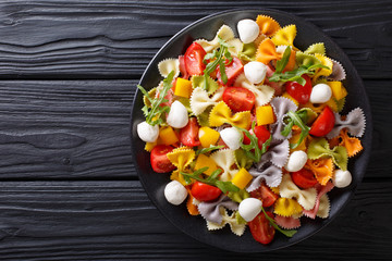 Warm salad of farfalle pasta, tomatoes, arugula and mozzarella closeup. horizontal top view