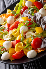 Warm salad of farfalle pasta, tomatoes, arugula and mozzarella closeup. vertical