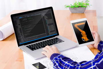 Software engineer's workplace. Engineer's hands working on laptop and holding tablet with kuka on...