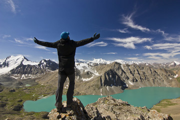 man in black jacket standing with hands-up above blue lake in mountains