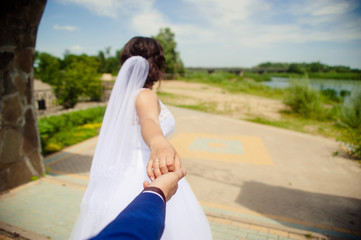 Fototapeta na wymiar Beautiful young woman bride holds the hand of a man in outdoors. Follow me