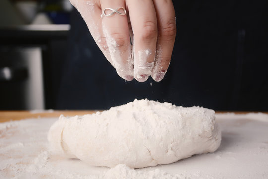 Woman hand adding flour to dough.
