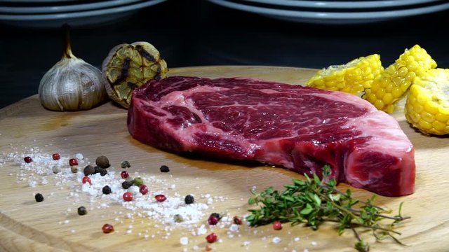 Raw meat. A large piece of beef chop on a cutting board with rosemary and spices.